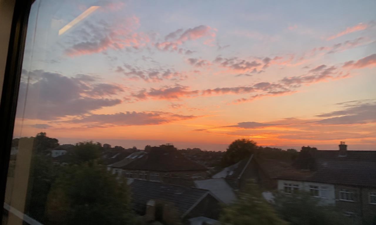 Un ciel pâle et doré au-dessus des toits, aperçu depuis la vitre d'un wagon au petit matin.